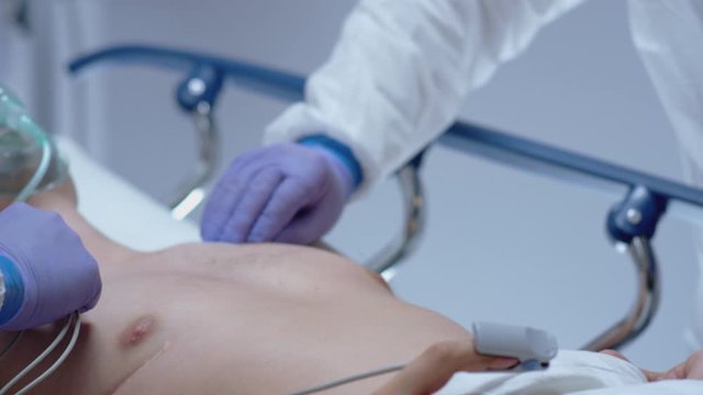 Doctors in Protective Suits Attaching ECG Leads to Coronavirus Patient - Medium Tilting Shot