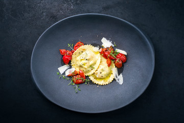 Traditional Italian ravioli pasta offered with parmesan cheese and fried tomatoes as top view on a modern design plate with copy space