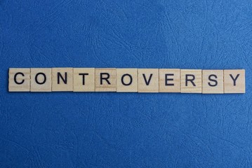 word contoversy from small gray wooden letters lies on a blue background