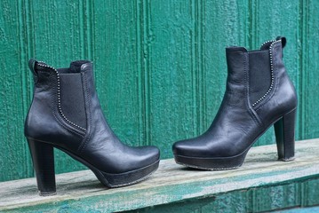 two black women leather boots stand on a gray wooden board against a green wall