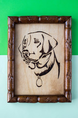 Wooden picture with the image of a dog made using the technique of pyrography and decorated with a carved frame