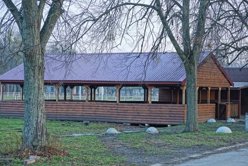 a large brown wooden arbor stands outside among the trees on the edge of the field