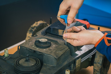 Serviceman stripping robotic lawnmower with imbus tool, motorized lawnmower being serviced on a...