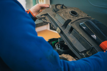 Serviceman stripping and opening up robotic lawnmower, motorized lawnmower being serviced on a...