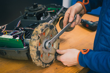 Serviceman stripping and removing wheels on robotic lawnmower, motorized lawnmower being serviced...