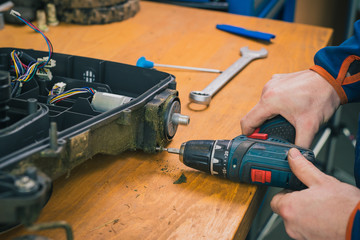 Serviceman stripping and removing electric motors on robotic lawnmower, motorized lawnmower being...