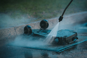 Man cleaning the underside of a robotic autonomous lawnmower with the help of a high pressure jet cleaner as part of a service plan. Gunk flying out.