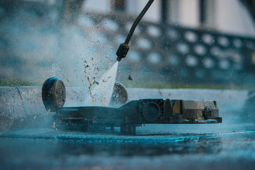 Man cleaning the underside of a robotic autonomous lawnmower with the help of a high pressure jet...
