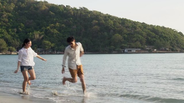 Happy asian couple walking with romantic and holding hand on the beach in summer for leisure together, man and woman stroll and playing water in vacation for honeymoon, holiday and travel concept.