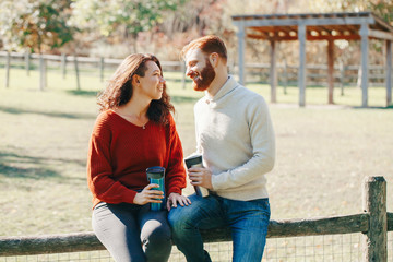 Happy couple man and woman in love sitting in park outdoor. Lovely beautiful Caucasian heterosexual people dating on an autumn fall summer day. Adult people hold tea coffee drink mugs.