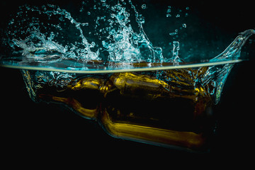 Brown beer bottle falls into water making big splash of drops and spray on a dark background. Juicy and fresh concept of refreshing drink in water.