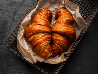 two big delicious croissants on parchment on a dark concrete background