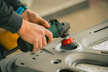 Young service man is using an angle grinder with a wire brush to clean the underside of an old vintage car about to be restored