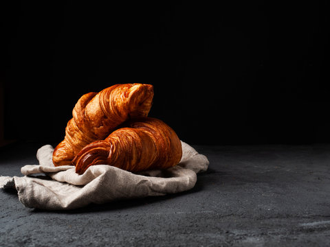 two golden croissants on a linen cloth on a dark background with free text space