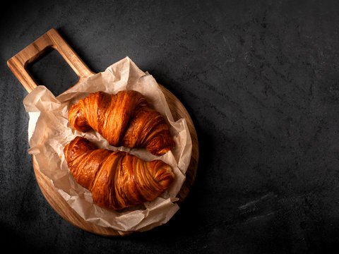 two big delicious croissants on a wooden board on a dark concrete background. Top view. Free text space