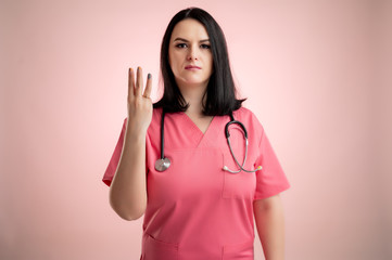 Beautiful woman doctor with stethoscope, wearing pink scrubs counting three with her fingers