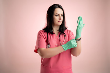 Beautiful woman doctor with stethoscope, wearing pink scrubs takes medical gloves on her hands