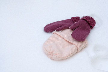 pink knitted hat and two mittens in the snow. Women's hat and warm mittens in winter.