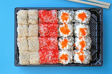 Sushi set in black plastic packaging top view. Sushi of different types on a blue background. Sushi with caviar, sesame seeds and Philadelphia cheese. A quick snack at work, food delivery.