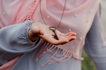 The girl in a scarf holds a necklace with a key in her hands