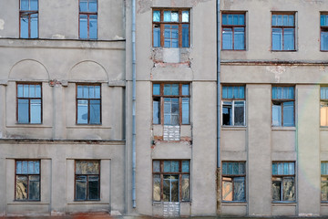 Old building facade with broken windows. Gray multi-storey building with windows of different sizes. Abandoned building with wooden frames for windows.