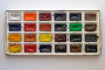 Sets of art paints in a plastic box top view. Watercolor paints in the package on a white background. Different colors of paints in containers. Old used dirty watercolor.