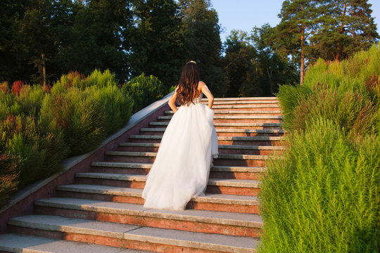 bride in a white beautiful dress climbs the steps in the garden, lovely girl