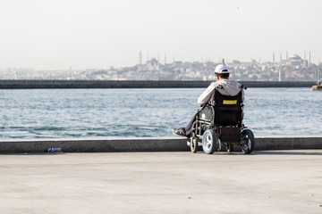 Man standing by the sea with his wheelchair. We watch the sea and we are alone.