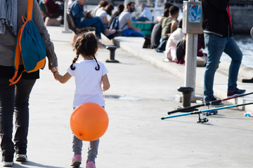 The orange balloon is walking in the child's hand and with his mother on the street.