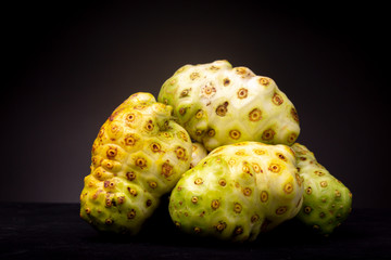 Noni or Cheese Fruit grouped together with various colour shades contrasted against a dark background