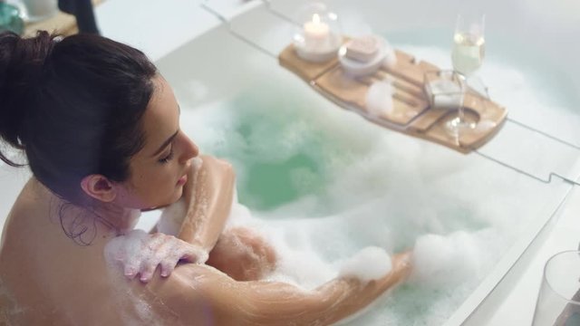 Smiling woman washing hands with foam. Sexy girl relaxing in bath with candles