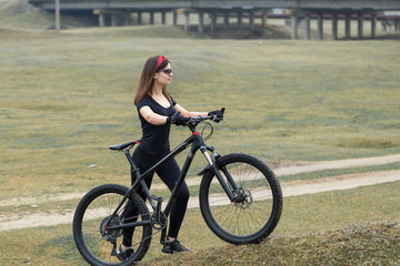 Obraz na płótnie Canvas Girl on a mountain bike on offroad, beautiful portrait of a cyclist in rainy weather, Fitness girl rides a modern carbon fiber mountain bike in sportswear. Close-up portrait of a girl in red bandana.