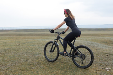 Girl on a mountain bike on offroad, beautiful portrait of a cyclist in rainy weather, Fitness girl rides a modern carbon fiber mountain bike in sportswear. Close-up portrait of a girl in red bandana.