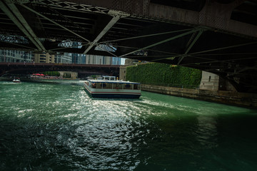 Sightseeing boat traveling on the Chicago river seen as it passes from under a steel bridge.