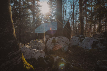 Old army barracks or cottages hiding in the depths of forest at Kocevje or Kocevski rog. Partisan hideout in Slovenia called Baza 20 on a sunny winter day. Visible two of cabins. - obrazy, fototapety, plakaty