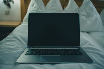 Frontal view of a laptop keyboard sitting on a bed in hotel room. Vintage hotel room with laptop on the sheet. Concept of online hotel booking.