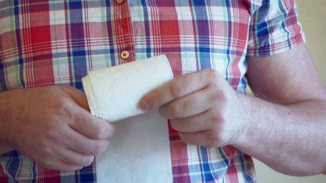 Men's hands unwind a roll of white toilet paper.
