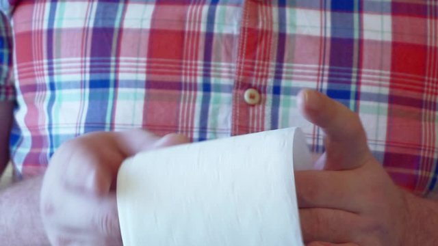Men's hands unwind a roll of white toilet paper.
