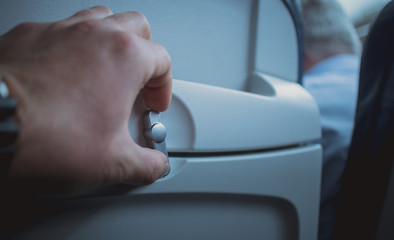 Man opening knob for releasing table tray on an aeroplane seat backrest. Visible tray in stowed...