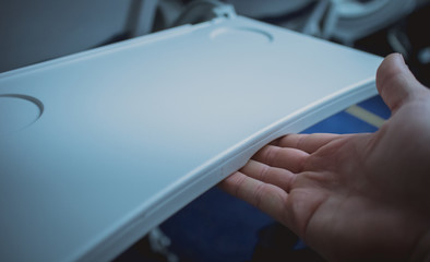 Man closing or stowing table tray on an aeroplane seat backrest. Visible tray in open position with...