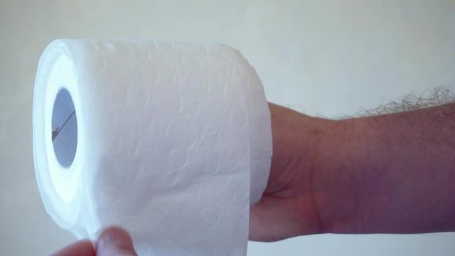 Men's hands unwind a roll of white toilet paper