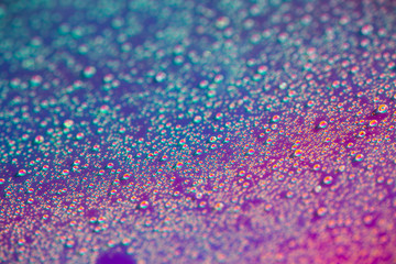 A lot of small drops of water on a colorful pastel holographic background.
