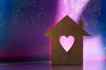 Obraz na płótnie Canvas Wooden icon of house with hole in the form of heart on pink and purple dark galactic background with light bokeh.