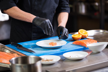Theme cooking is a profession of cooking. Close-up of a Caucasian man's hand in a restaurant kitchen preparing red fish fillets salmon meat in black latex gloves uniform