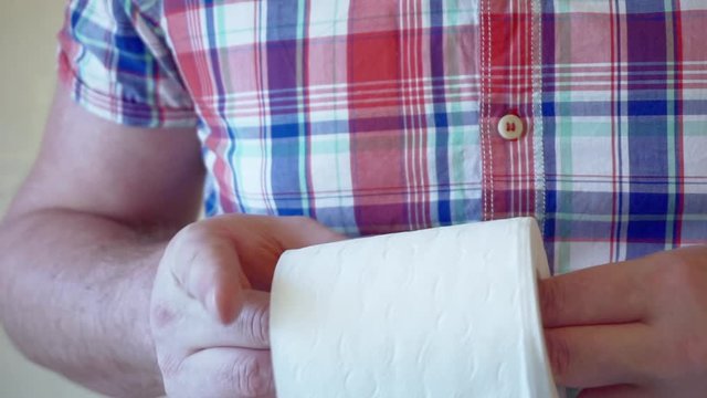 male hands hold a roll of white toilet paper.