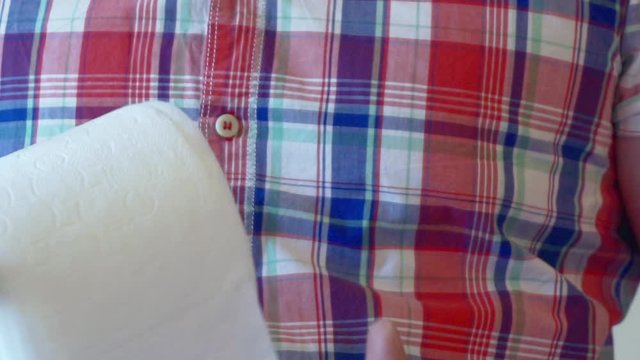Men's hands unwind a roll of white toilet paper.