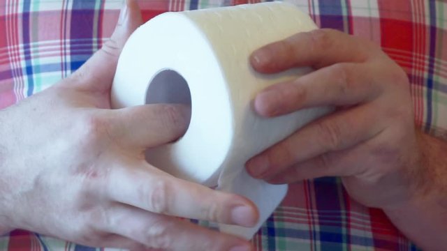 Men's hands unwind a roll of white toilet paper