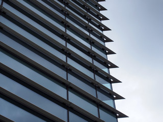 corner of a futuristic building with steel geometric lines and blue glass windows reflecting a blue...