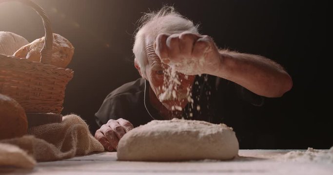 Professional mature caucasian baker putting flour on loaf of bread dough with passion, retired pensioneer enjoying his new hobby, isolated on black background 4k footage