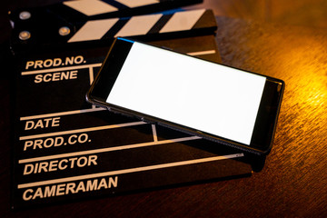 mobile phone with empty white bright screen movie clapper board. Concept of streaming TV on...
